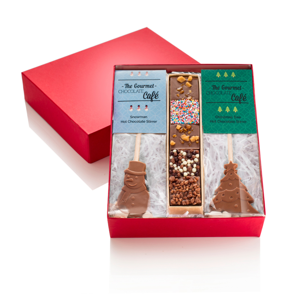 Festive red gift box filled with a snowman hot chocolate stick, a christmas tree hot chocolate stick, and chocolate mendiants.